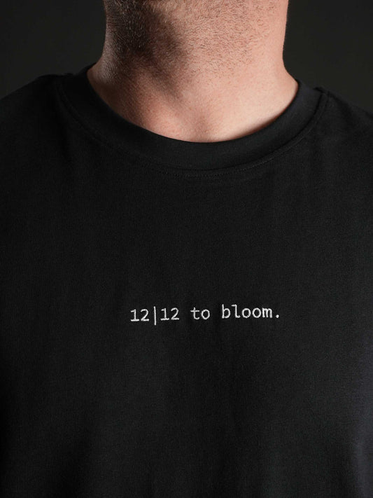 Nahaufnahme des gestickten ‚12|12 to bloom‘ Schriftzugs auf dem schwarzen T-Shirt