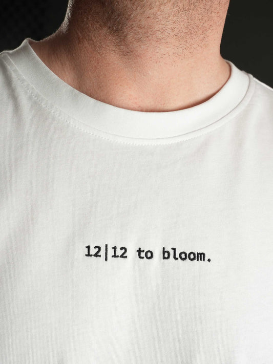 Nahaufnahme des gestickten ‚12|12 to bloom‘ Schriftzugs auf dem weißen T-Shirt.