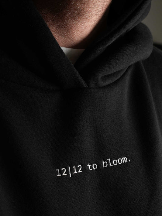 Nahaufnahme des hochwertigen Stickmotivs ‚12|12 to bloom‘ auf der Vorderseite des Hoodies.