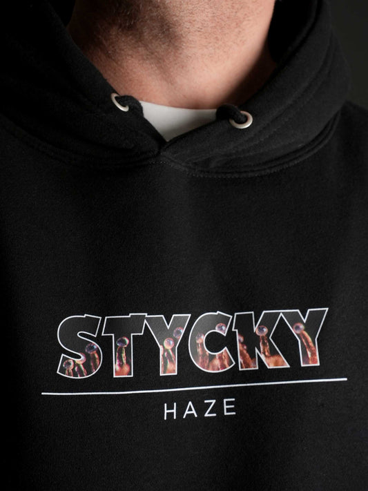 Nahaufnahme des ‚STYCKY Haze‘ Prints auf dem schwarzen Hoodie